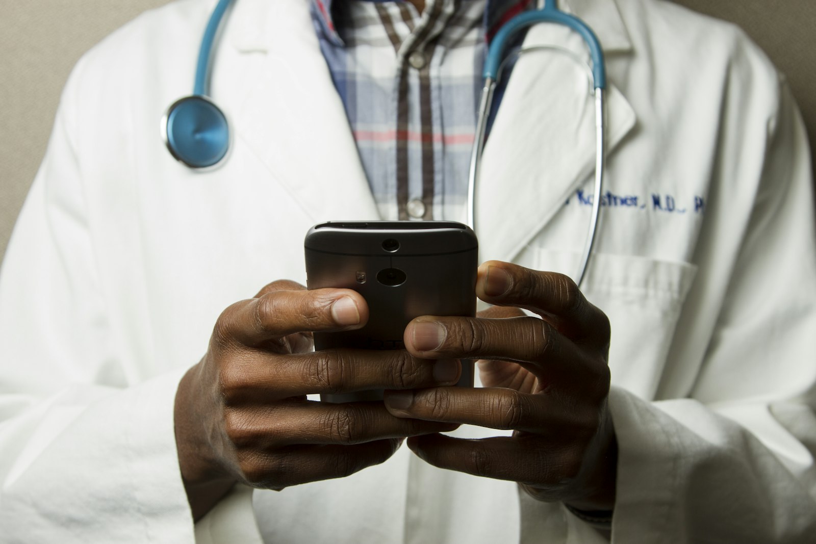 A physician in a white coat reviewing information on a phone